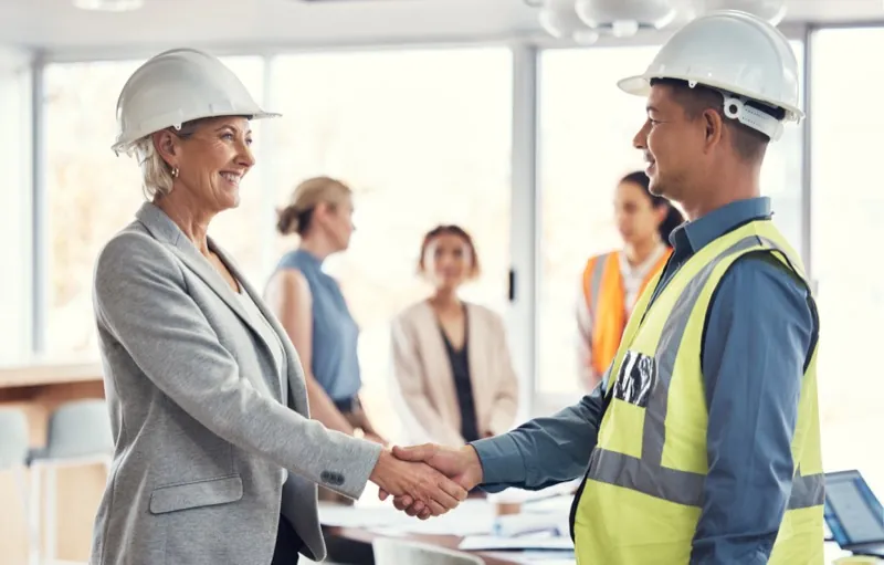 Staffing agency manager shaking hands with a placed construction worker on site — staffing agency time tracking
